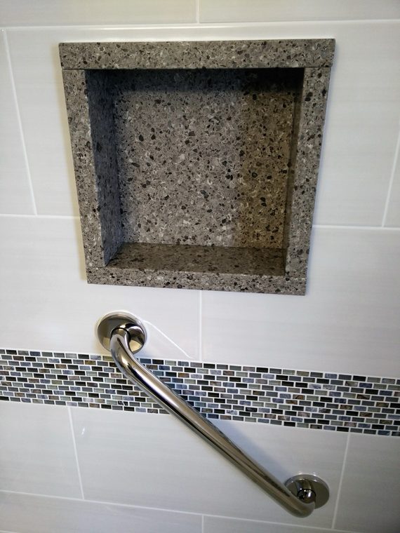 Stone shower niche with a mosaic band and a grab bar below