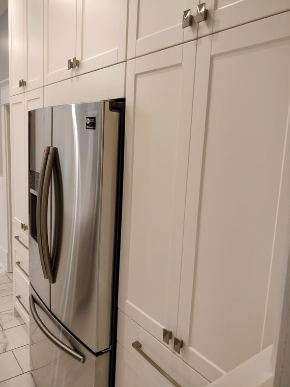 Full height white cabinetry beside a stainless fridge